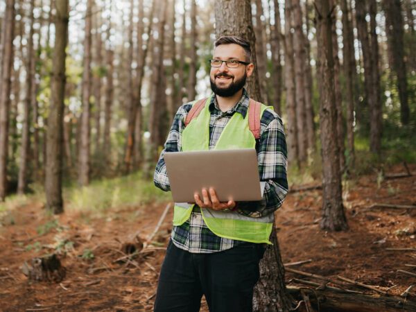Man with laptop stood in forest
